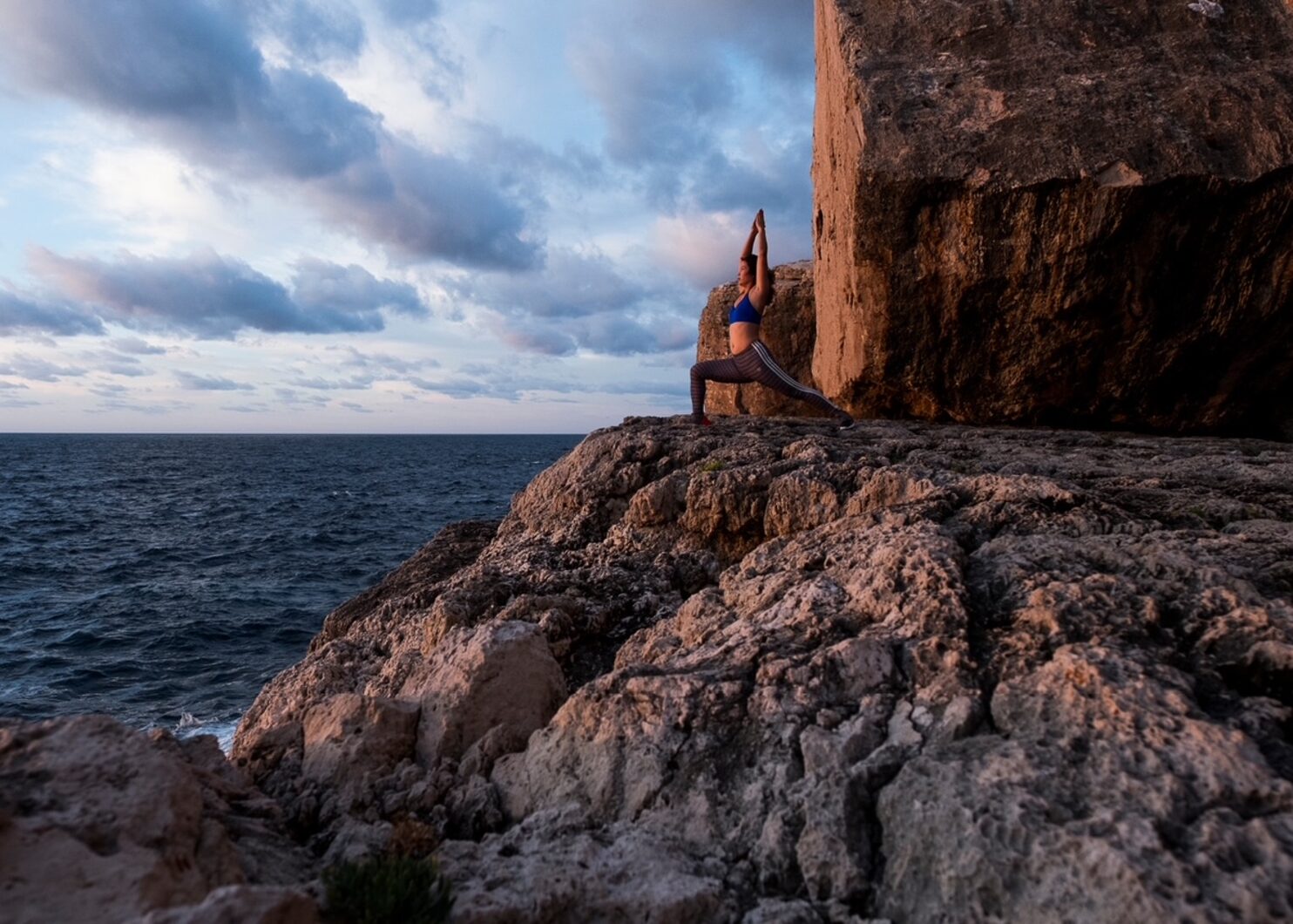 Janet in Yoga-Kriegerpose auf einer Felsklippe am Meer, Abendstimmung